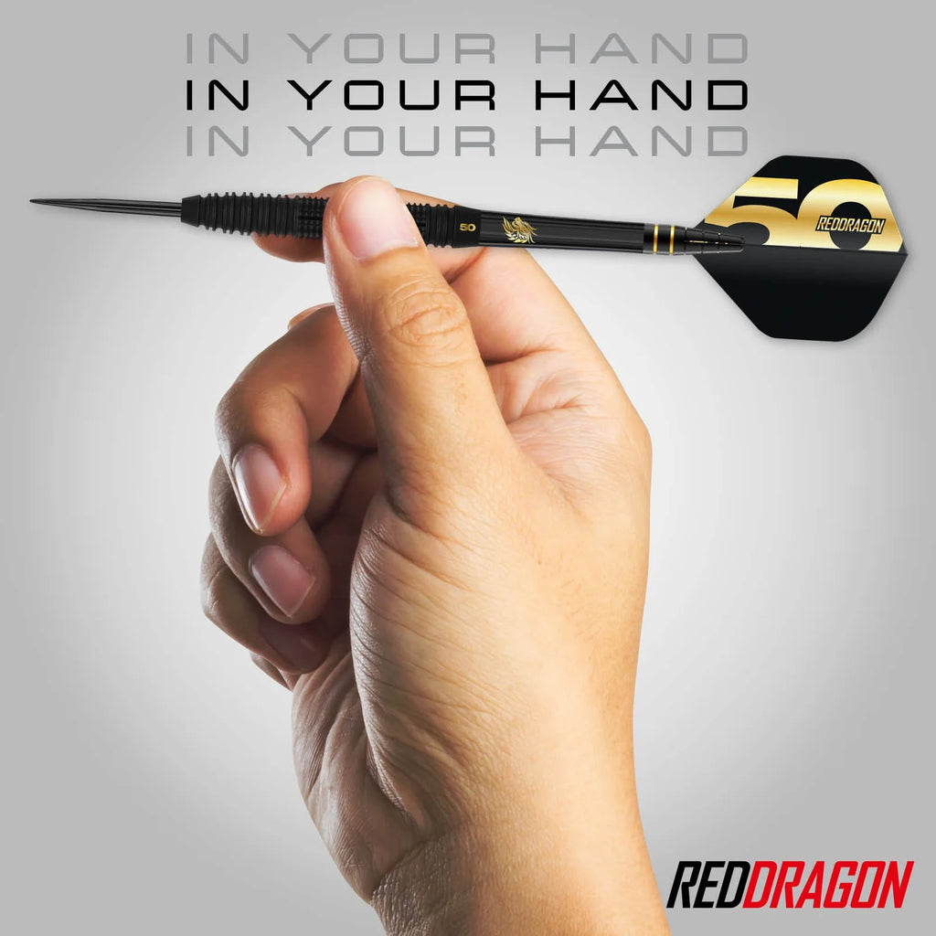A hand holds a 90% tungsten Jonny Clayton 50 Year Player Edition Box dart from Professional Darts Corporation before a gray background, with "IN YOUR HAND" repeated above and the RedDragon logo in the bottom right corner.